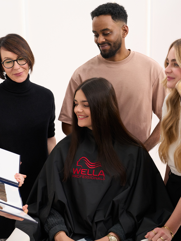 a model in a Wella Professionals apron and a group of hairdressers look at a color sample collection