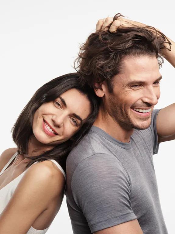 The man holds a handful of his own strong hair in his grip, the smiling woman leans against his back