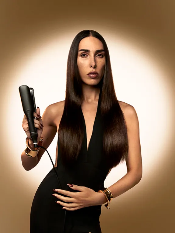 Brunette holding ghd hair styler; golden brown background with circle of light in the center