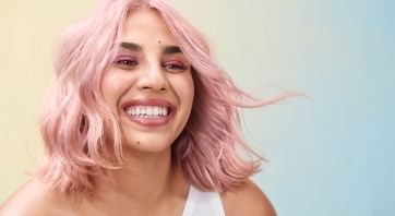 Smiling woman with pink hair on a yellow and blue gradient background