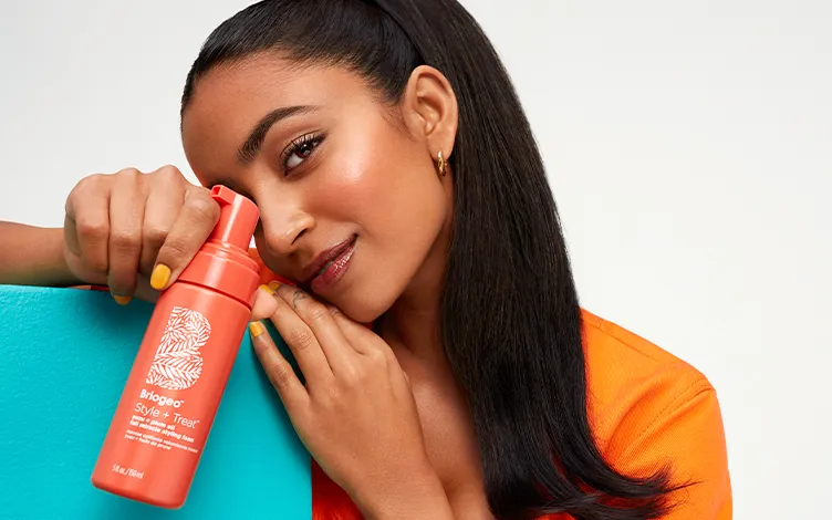 WellaCompany-deib-OurProductsAndServices-Card.jpg smiling black-haired woman holding an orange bottle of Styling Foam