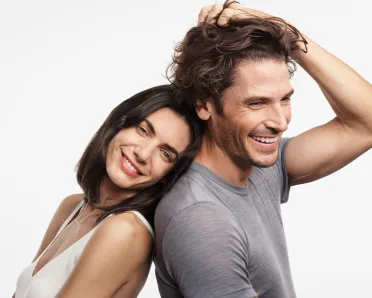 The man holds a handful of his own strong hair in his grip, the smiling woman leans against his back
